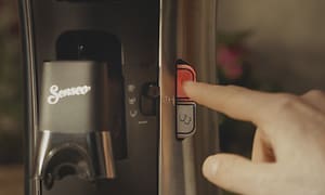 Närbild på en hand som trycker på på-knappen på en Senseo Select kaffemaskin