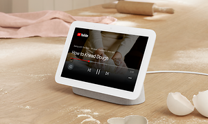 Vit Google Nest Hub-enhet på ett bord, visar YouTube på skärmen.