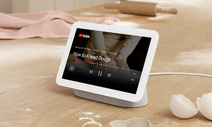 Vit Google Nest Hub-enhet på ett bord, visar YouTube på skärmen. 