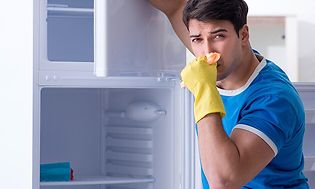 Man i blå t-shirt och gula diskhandskar städar ur ett kylskåp som luktar illa. 