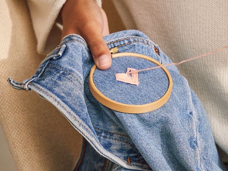 Kvinna som reparerar ett par jeans genom att sy ett hjärta