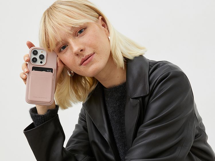 Kvinna som lutar sig mot sin telefon som har IDEAL OF SWEDEN plånboksfodral