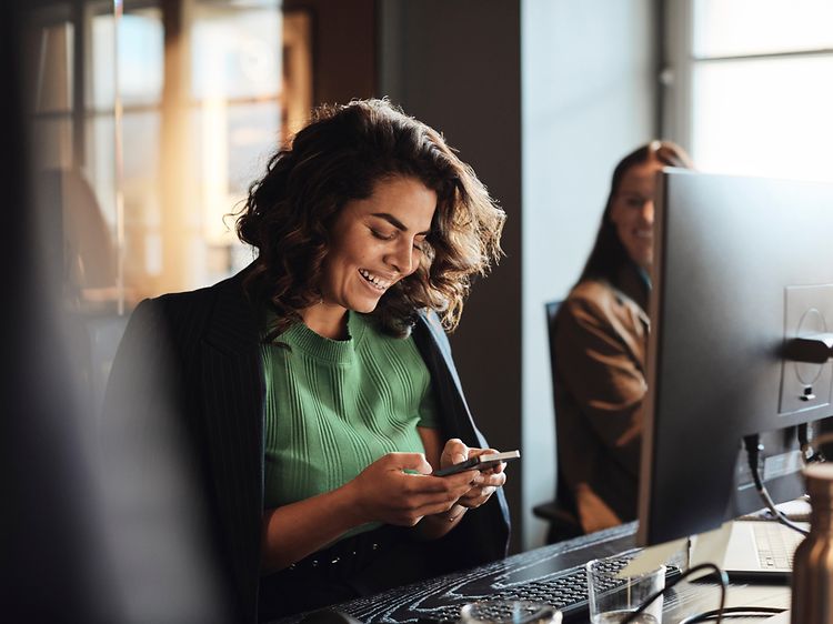 Digital cleanup - Woman with a smartphone in front of a PC in an office