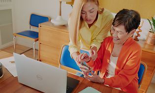 Två kvinnor framför en bärbar dator och en smartphone