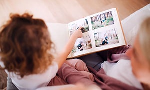 En kvinna och ett barn sitter sitter och tittar på foton i ett fotoalbum, barnet pekar på en av bilderna.