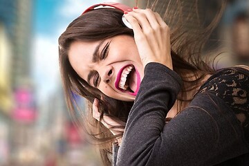 Kvinna med rosa läppstift diggar till musiken i ett par röda hörlurar, i bakgrunden syns en blurrig stadsmiljö. 