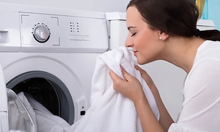 En kvinna håller upp en nytvättad vit handduk från torktumlaren och luktar på den. 