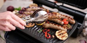 Man grilling sausages and vegetables on electric grill