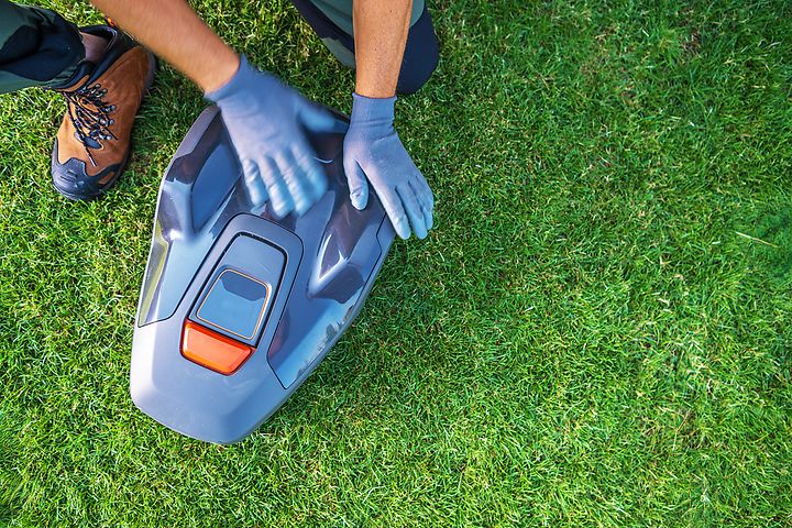 A Person Services a Robotic Lawn Mower on a Lush Green Lawn During Daylight