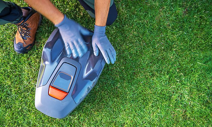 A Person Services a Robotic Lawn Mower on a Lush Green Lawn During Daylight