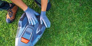 A Person Services a Robotic Lawn Mower on a Lush Green Lawn During Daylight