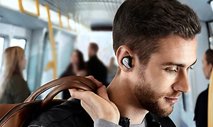 Man på tunnelbanan med en brun väska slängd över ena axeln, har på sig svarta helt trådlösa in-ear hörlurar.