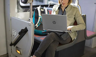 Kvinna sitter på tåget och jobbar med en HP laptop i knät. På sätet bredvid står en ryggsäck.
