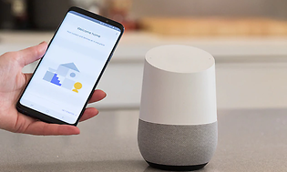En hand håller i en mobiltelefon och kopplar till Google Home.