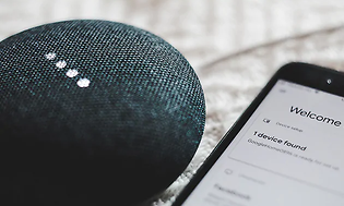 Närbild på en Google Home mini-enhet med en iphone bredvid.