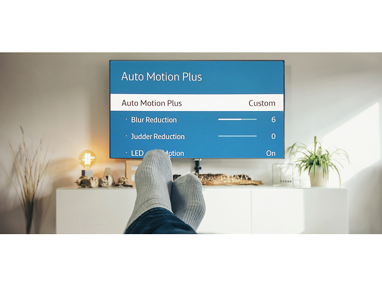 Bilden visar en stor TV med meny-sida "auto motion plus" och i förgrunden två fötter med grå sockar.