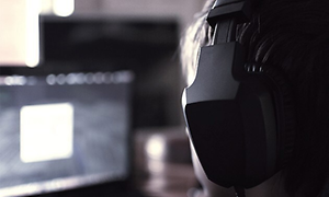 Bild från sidan på en person med stort svart headset som ser på en skärm som är oskarp i bakgrunden.
