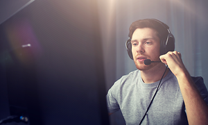 Stor skärm i förgrunden, man med headset och mikrofon sitter och ät toalt fokuserad på det som sker på skärmen.