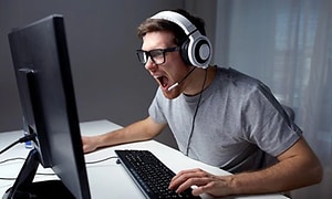 Man som sitter framför en dator och har headset med mikrofon på sig och skriker åt skärmen, totalt fokuserad på det som sker. 