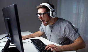 Man som sitter framför en dator och har headset med mikrofon på sig och skriker åt skärmen, totalt fokuserad på det som sker.