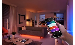 Hand håller upp en mobiltelefon med meny i ett mörkt rum, för att visa att du kan styra lamporna med en app. 