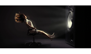 En kvinna som sitter på en kontorsstol med hjul i ett mörkt rum framför gigantisk subwoofer och är på väg att blåsa bort.