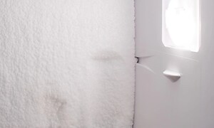 Insidan av ett tomt kylskåp med is eller frost längs med hela innerväggen. 