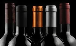 Mörk bild på toppen av fem olika vinflaskor med olika etikett i olika färg. Svart bakgrund. 