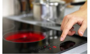 EN hand justerar värmen på en induktionshäll där en rund röd markering lyser för att visa att plattan är varm. 