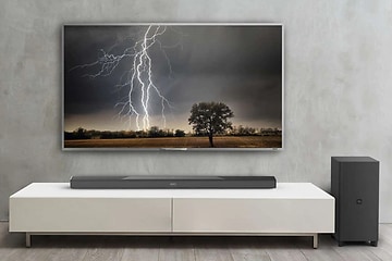 Stor TV uppsatt på väggen med bild på en åskblixt. Tillhörande högtalare vid sidan och soundbar placerad på en vit TV-bänk.