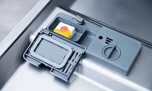 Närbild på diskmedelsfacket på en diskmaskin där det ligger en tablett, redo att sättas på.  