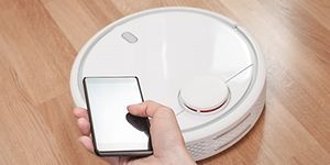 Någon styr en vit robotdammsugare från sin mobiltelefon.