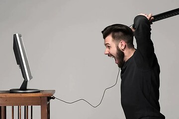 Man med ett tangentbord i högsta hugg, på väg att slå det i datorn som står framför på ett bord. 