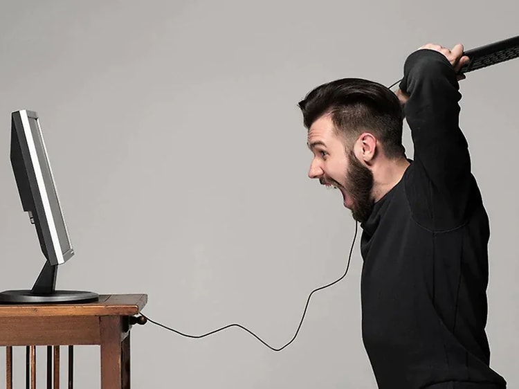 Man med ett tangentbord i högsta hugg, på väg att slå det i datorn som står framför på ett bord. 
