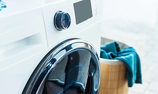 Närbild på fronten av en kombinerad tvättmaskin och torktumlare. Bredvid står en tvättkorg med smutstvätt. 
