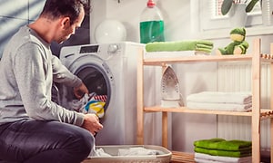 Man i en prydlig tvättstuga stoppar in smutsig tvätt i olika fär i en kombinerad tvättmaskin med torktumlare. 