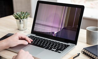 En MacBook (bärbar dator) med en trasig skärm ståendes på ett skrivbord.