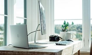 En bärbar dator som är ansluten till en skärm och tangentbord  på ett skrivbord.