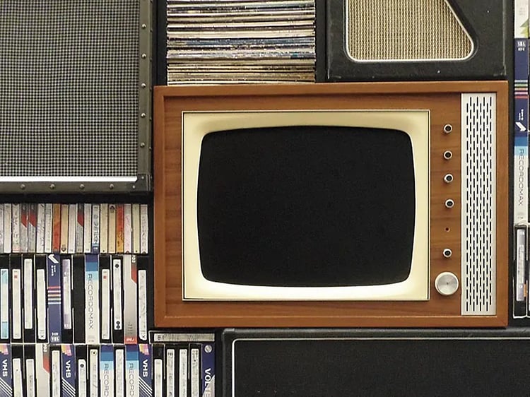 Retro TV i brun färg placerad i en bokhylla fylld med VHS-kassetter. 