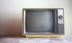 Gammal liten tjock-TV med ljus gul baksida, placerad på ett bord. 