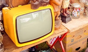 Illgul gammal tjock-TV till salu på en loppmarknad, står på ett träbord med massa andra prylar. 