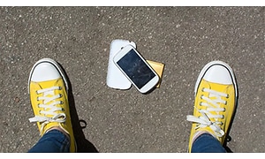 En tappad mobiltelefon ligger på marken och skärmen är trasig.