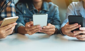 Tre unga personer sitter med sina smartphones i händerna.
