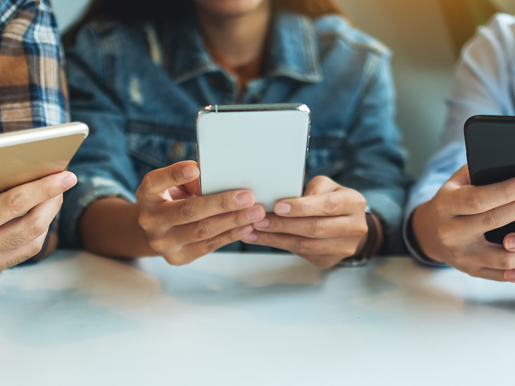 Tre unga personer sitter med sina smartphones i händerna.