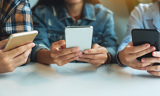 Tre unga personer sitter med sina smartphones i händerna.