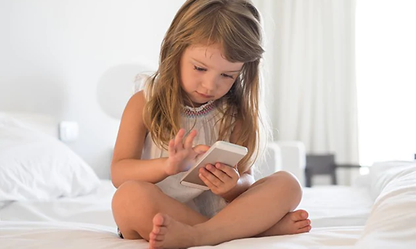 Ung flicka sitter i en säng och ser på en mobiltelefonen.