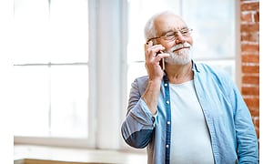 En äldre man talar i sin smartphone och ler.