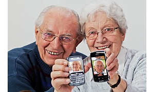 Ett äldre par med varsin smartphone som visar bilder av varandra.