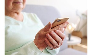 En äldre kvinna sitter med sin smartphone i handen.