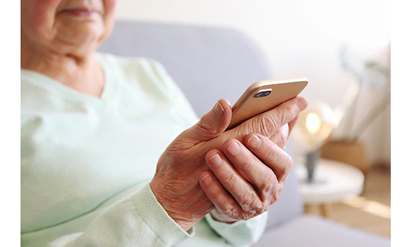 En äldre kvinna sitter med sin smartphone i handen.